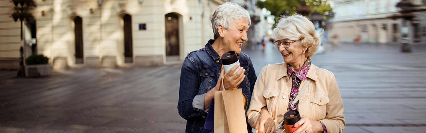 Two women holding hands outdoors while also holding cups and bags