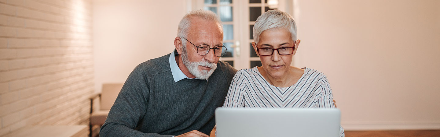 A couple sitting down at a desk and looking at a laptop